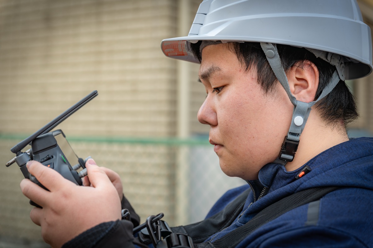 ヘルメット着用の受講生がDJI送信機を操作しながら画像データを確認している様子