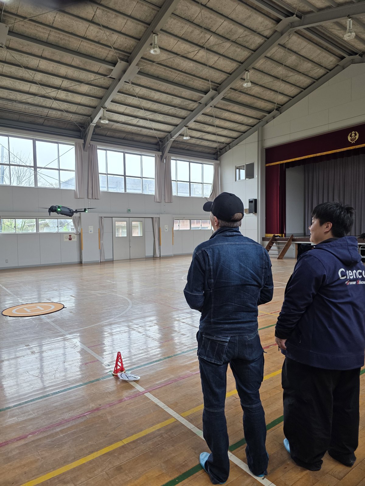 廃校施設を活用した体育館で受講者2名がドローンを操縦している様子